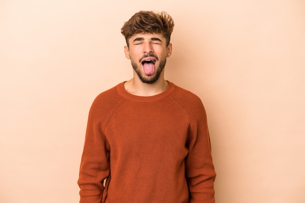 Young arab man isolated on beige background funny and friendly sticking out tongue.