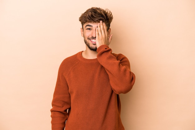 Young arab man isolated on beige background having fun covering half of face with palm.