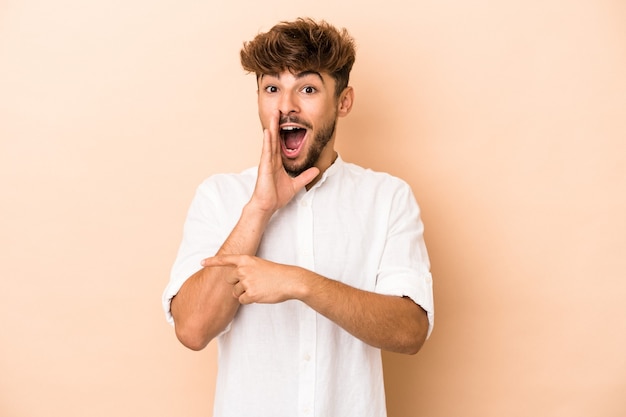 Young arab man isolated on beige background saying a gossip, pointing to side reporting something.