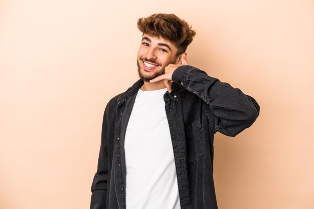 Young arab man isolated on beige background showing a mobile phone call gesture with fingers.