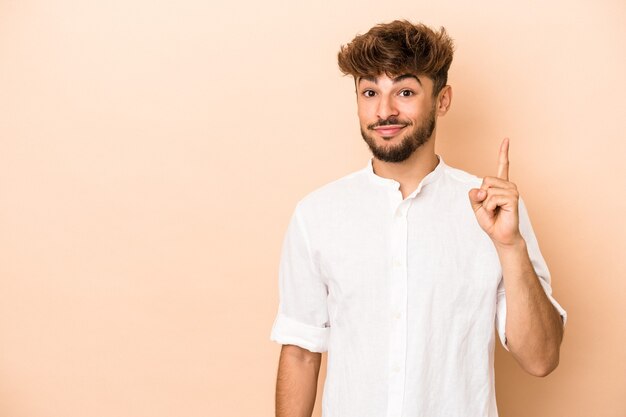 Young arab man isolated on beige background showing number one with finger.