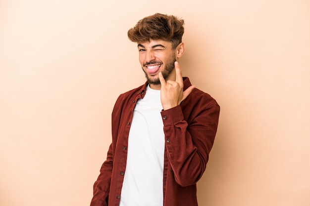 Young arab man isolated on beige background showing rock gesture with fingers