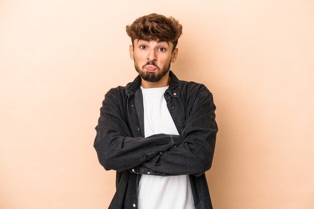 Young arab man isolated on beige background shrugs shoulders and open eyes confused.