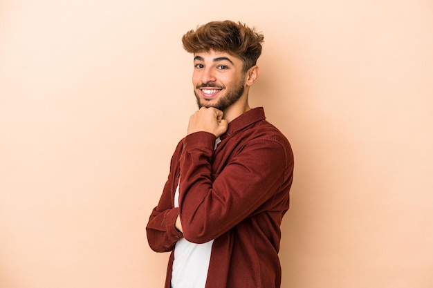 Young arab man isolated on beige background smiling happy and confident, touching chin with hand.