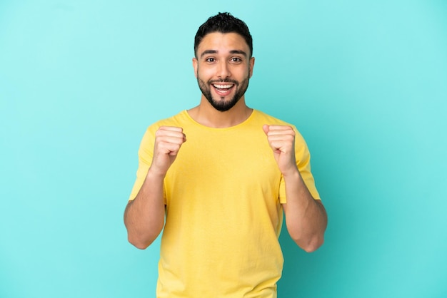 Young arab man isolated on blue background celebrating a victory in winner position