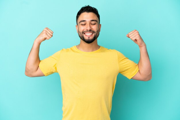 Young arab man isolated on blue background doing strong gesture