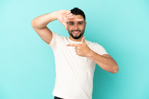 Young arab man isolated on blue background focusing face. Framing symbol