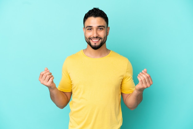 Young arab man isolated on blue background making money gesture