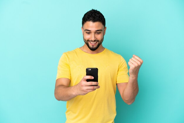 Young arab man isolated on blue background surprised and sending a message