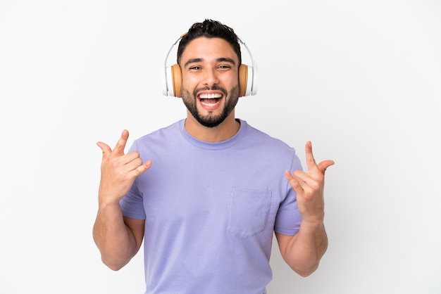 Young arab man isolated on white background listening music making rock gesture