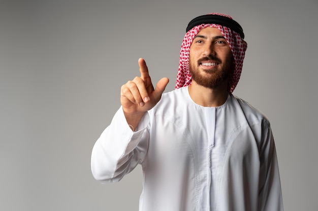 Young Arab man pointing hand to copy space on gray background