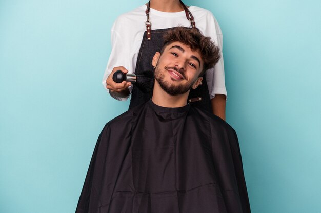 Giovane uomo arabo pronto a farsi tagliare i capelli isolato su sfondo blu