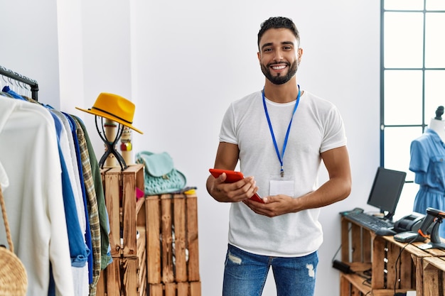 Young arab man shopkeeper using touchpad standing by clothes rack at clothing store