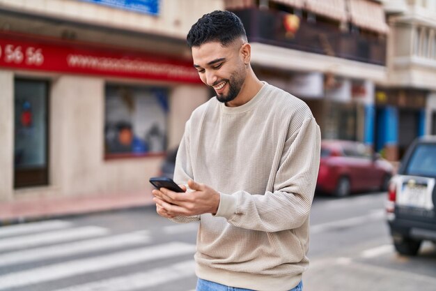 Young arab man smiling confident using smartphone at street