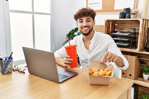 Young arab man using laptop having lunch at office