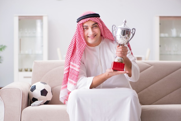 Young arab man watching football sitting on sofa