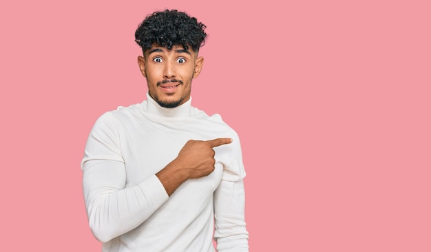 Young arab man wearing casual winter sweater pointing aside worried and nervous with forefinger, concerned and surprised expression