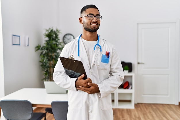 Foto giovane uomo arabo che indossa l'uniforme del medico che tiene appunti presso la clinica