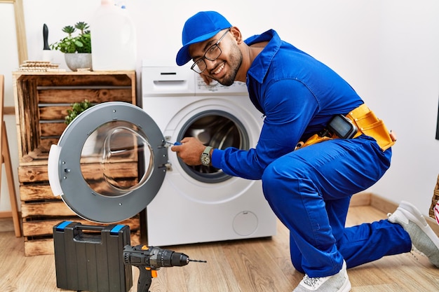 Young arab man wearing technician uniform repairing washing machine at laundry room