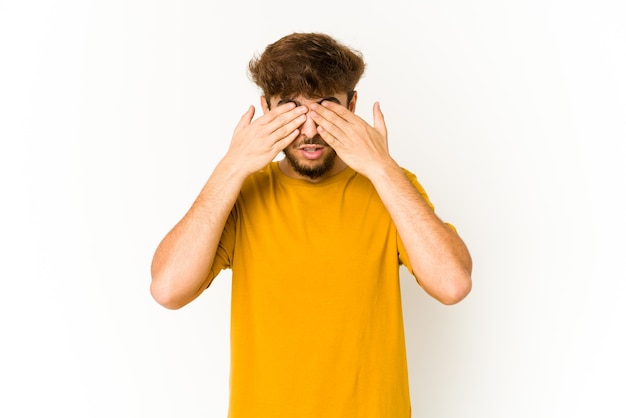 Young arab man on white afraid covering eyes with hands.