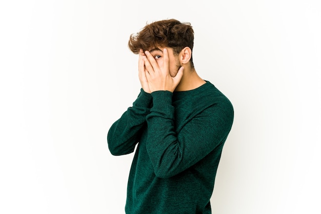 Young arab man on white blink through fingers frightened and nervous.