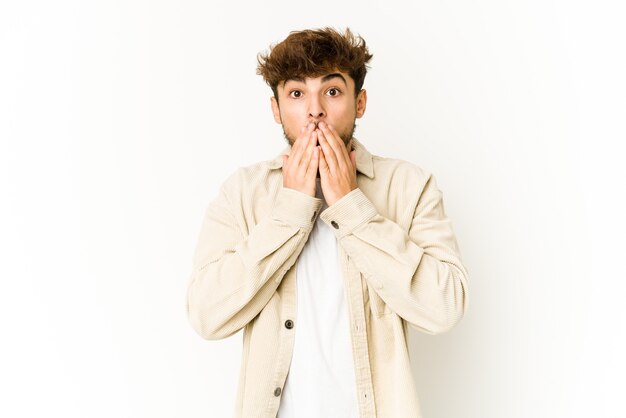 Young arab man on white shocked covering mouth with hands.