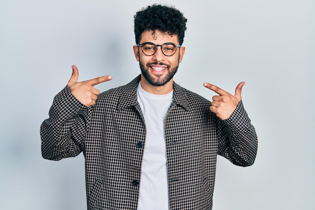 Young arab man with beard wearing glasses smiling cheerful showing and pointing with fingers teeth and mouth dental health concept