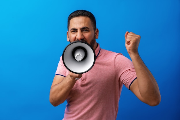 Young arab man with megaphone proclaiming something isolated on blue background