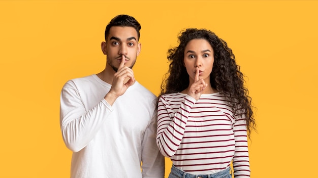 Young arab man and woman showing shh gesture at camera