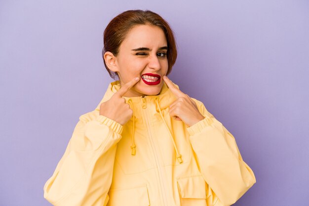 Young arab mixed race woman smiles, pointing fingers at mouth.