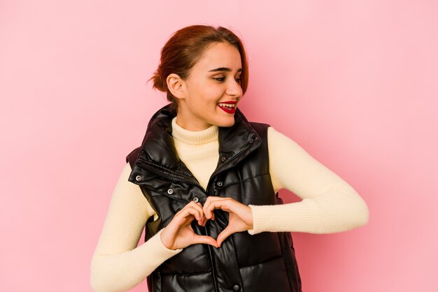 Young arab mixed race woman smiling and showing a heart shape with hands.