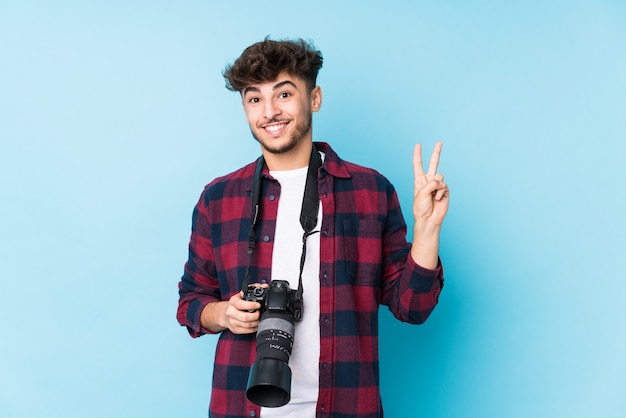 Young arab photographer man isolated joyful and carefree showing a peace symbol with fingers.