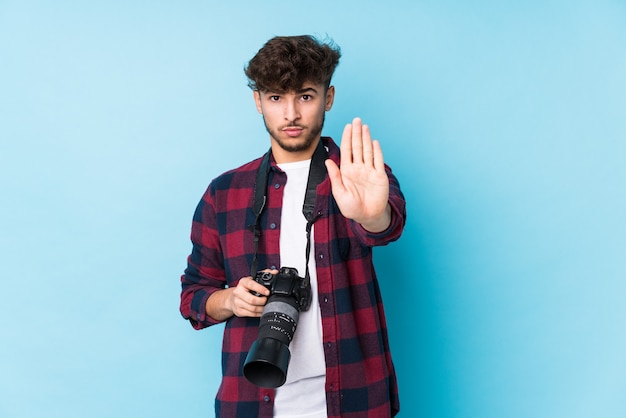 Young arab photographer man isolated standing with outstretched hand showing stop sign, preventing you.