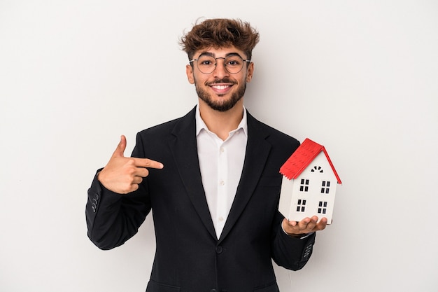 Young arab real estate man holding a model house isolated on isolated background person pointing by hand to a shirt copy space, proud and confident