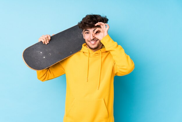 アラブのスケーターの若い男は、目で[ok]ジェスチャーを維持することに興奮しています。