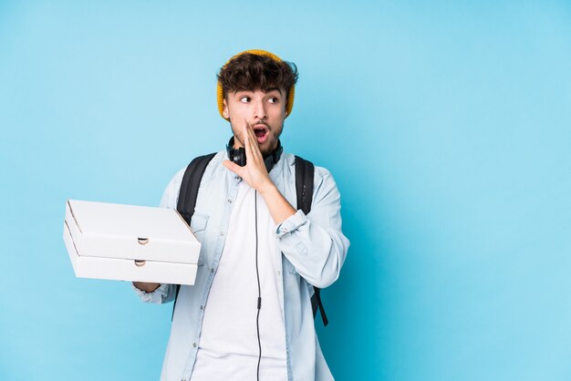 Young arab student man holding pizzas isolated is saying a secret hot braking news and looking aside