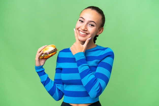 Young Arab woman holding a burger over isolated background happy and smiling