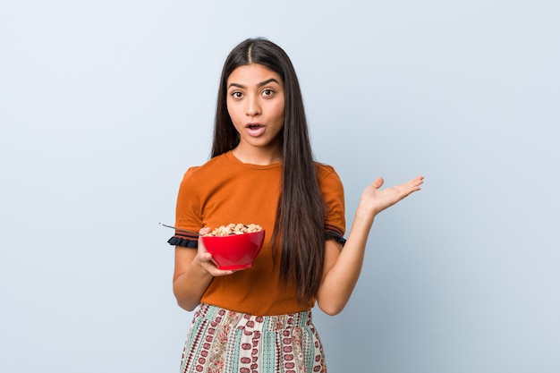 Young arab woman holding a cereal bowl impressed holding copy space on palm.