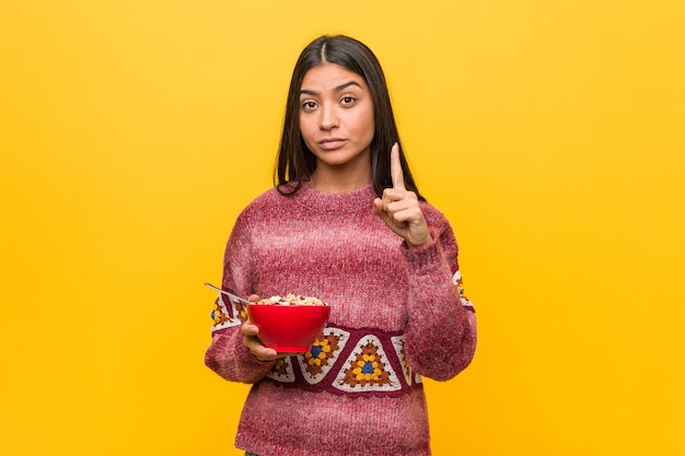 Foto giovane donna araba che tiene una ciotola di cereali che mostra il numero uno con il dito.