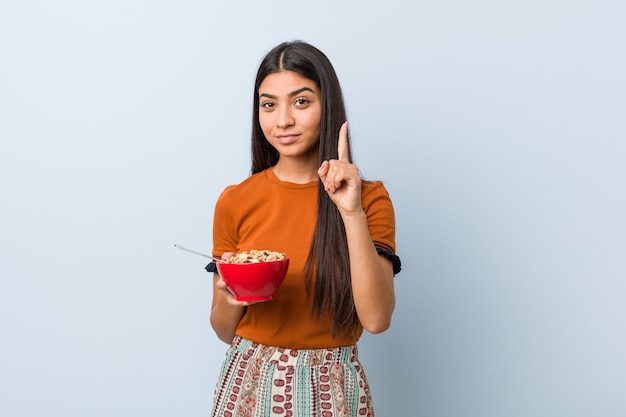 Young arab woman holding a cereal bowl showing number one with finger.