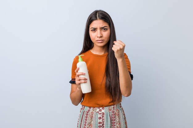 Young arab woman holding a cream bottle in  aggressive facial expression.