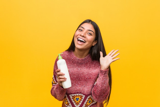 Young arab woman holding a cream bottle celebrating a victory or success