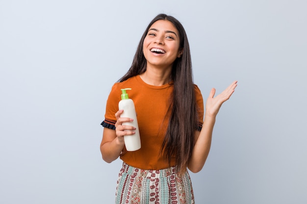 Young arab woman holding a cream bottle celebrating a victory