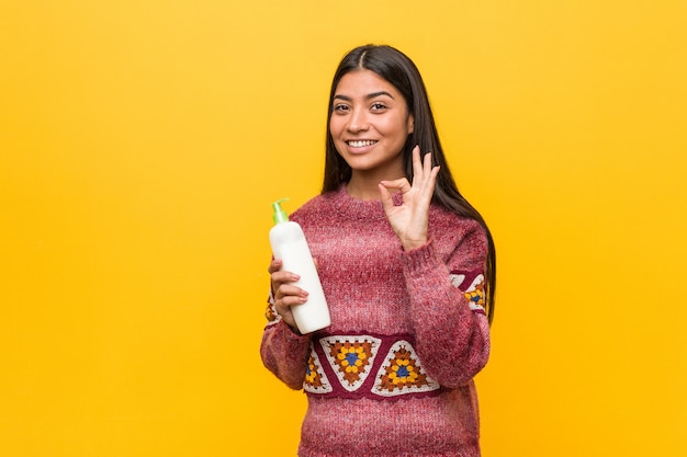 Young arab woman holding a cream bottle cheerful and confident showing ok gesture.