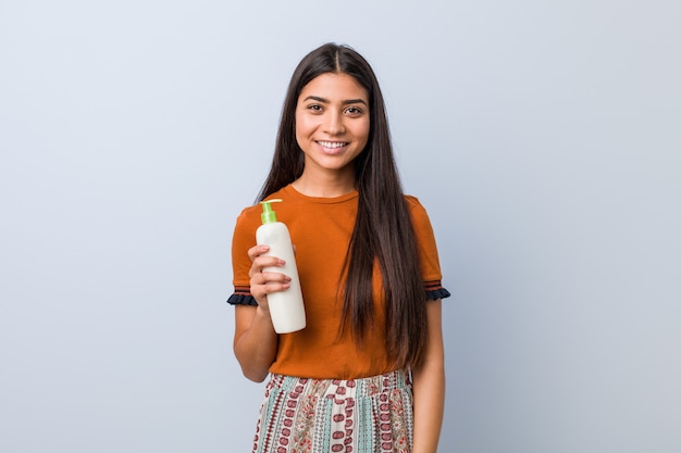 Young arab woman holding a cream bottle happy, smiling and cheerful.