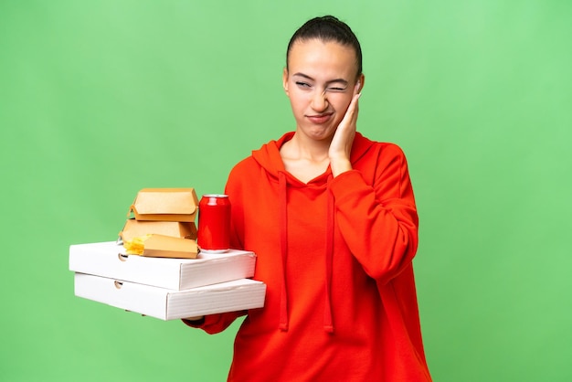 Young Arab woman holding fast food over isolated background frustrated and covering ears