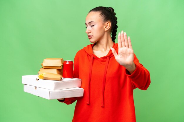 Photo young arab woman holding fast food over isolated background making stop gesture and disappointed