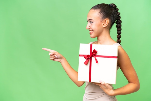 Young Arab woman holding a gift over isolated background pointing to the side to present a product