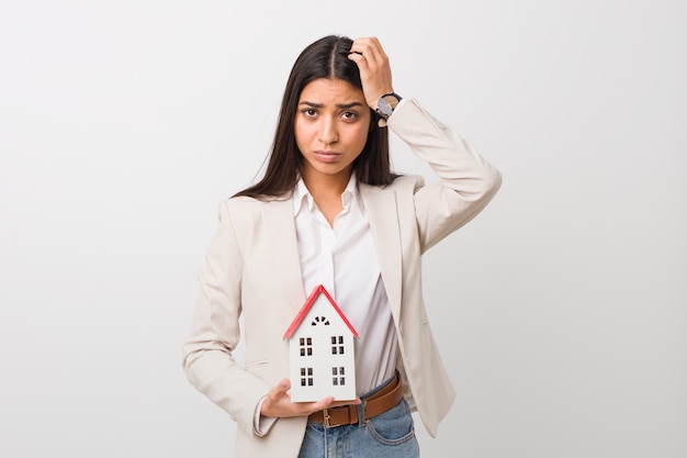 Young arab woman holding a house icon being shocked, she has remembered important meeting.