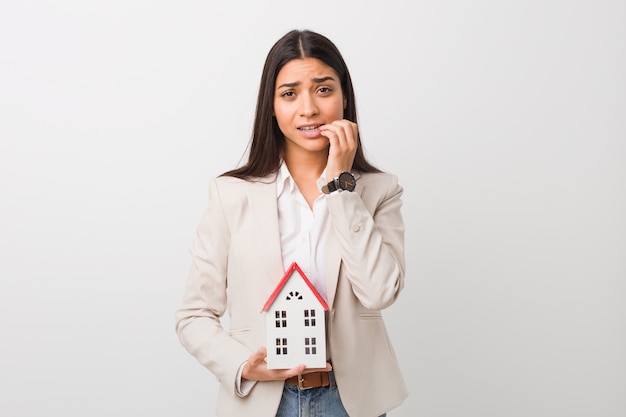 Young arab woman holding a house icon biting fingernails, nervous and very anxious.